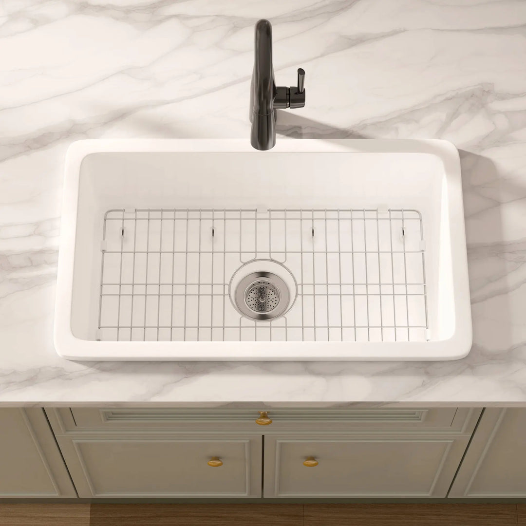 White rectangular drop-in fireclay kitchen sink with black faucet and grid