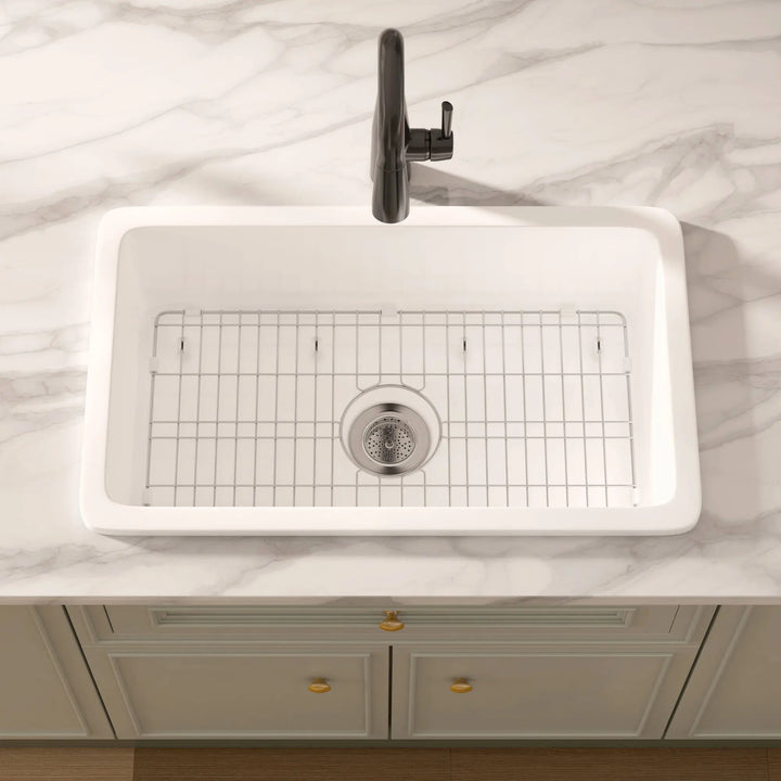 White rectangular drop-in fireclay kitchen sink with black faucet and grid