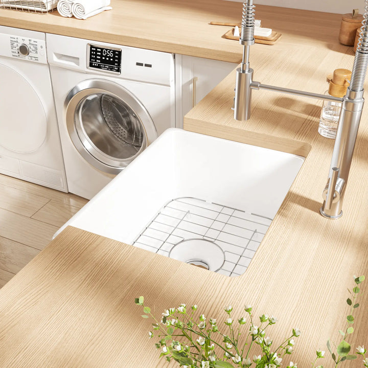 White farmhouse apron sink with grid rack in a laundry room setting