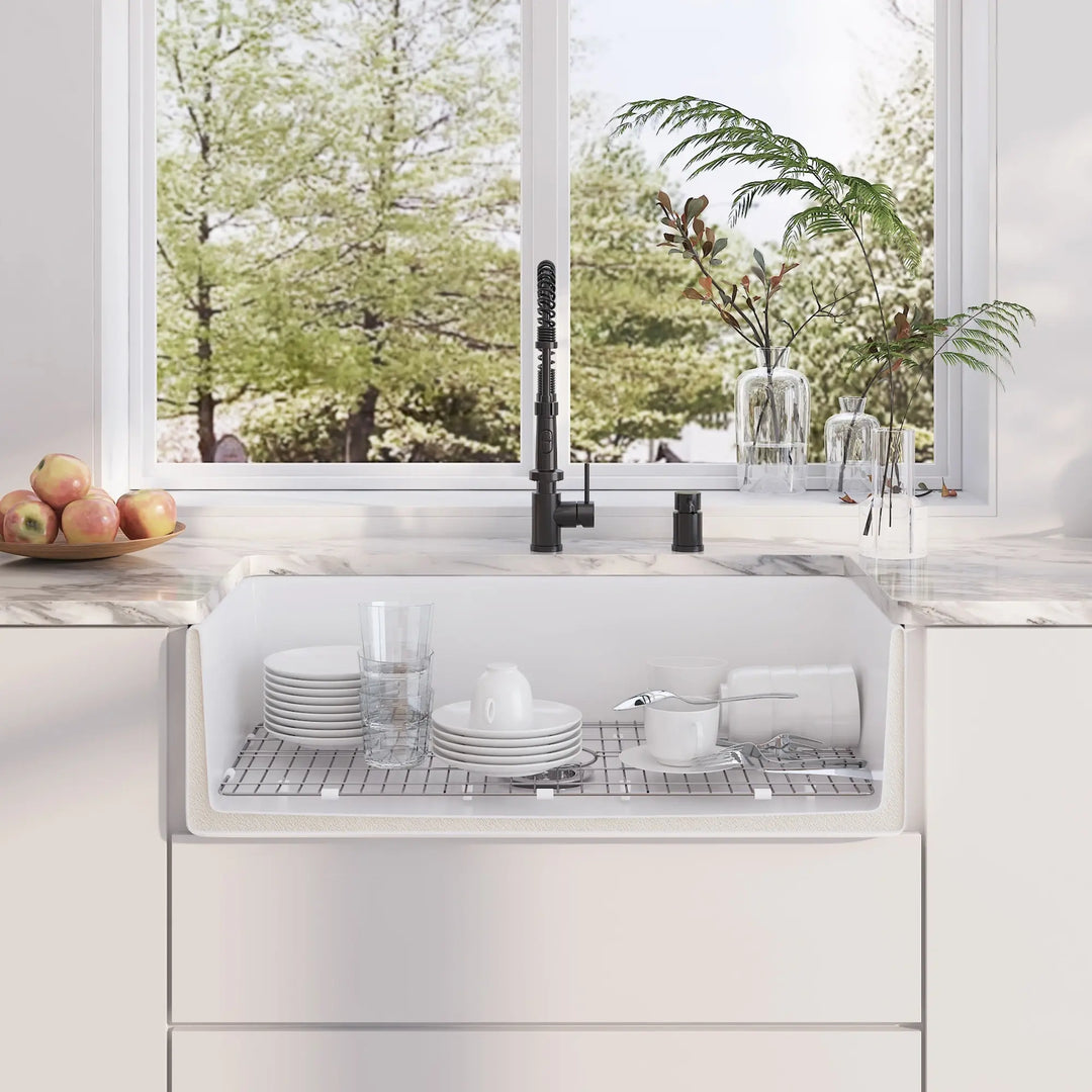 White fireclay farmhouse kitchen sink with stainless steel bottom rack holding tableware