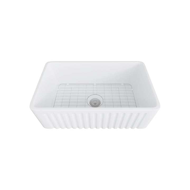 White fluted apron front fireclay farmhouse sink equipped with stainless steel bottom grid