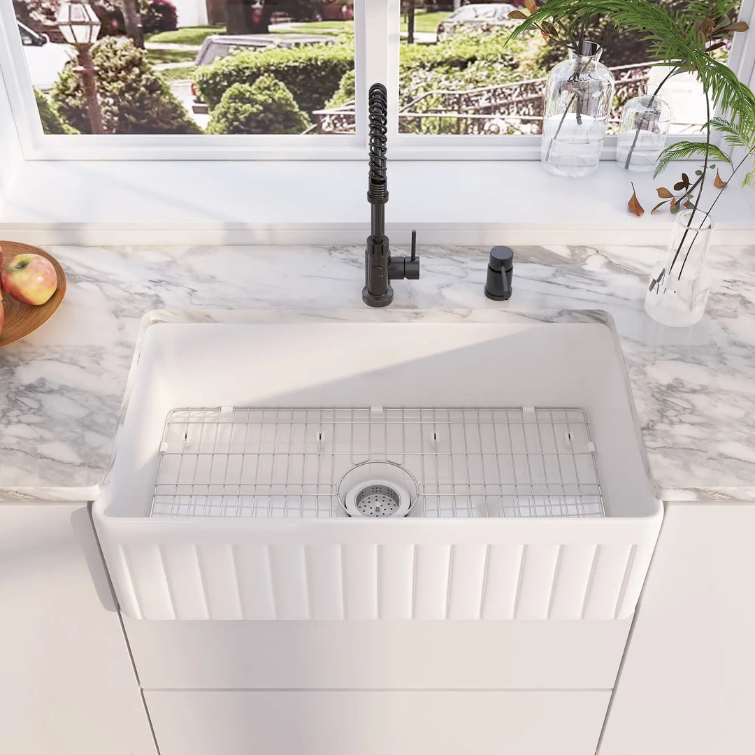 White fireclay farmhouse kitchen sink with front fluted design, stainless steel bottom grid, single bowl