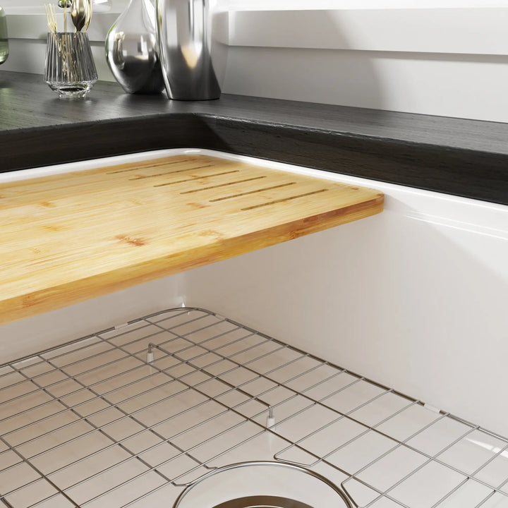 White fireclay kitchen sink interior fitted with bamboo cutting board and stainless steel bottom grid