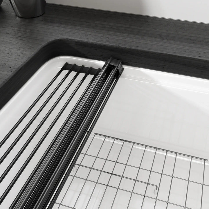 Rollable black metal dish drying rack and stainless steel bottom grid inside white fireclay kitchen sink