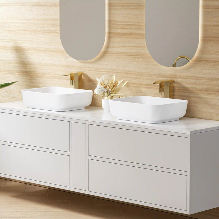 Two white rounded rectangular ceramic vessel sinks with brushed gold wall faucets