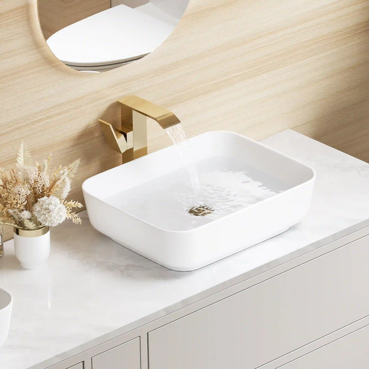 White square ceramic vessel sink with brushed gold wall-mounted faucet and gold drain