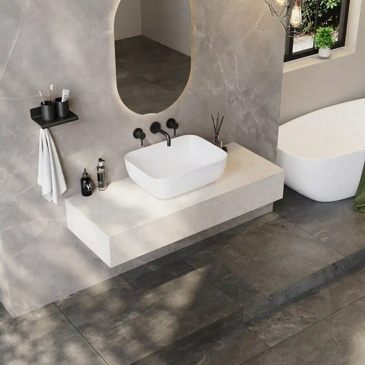 White rounded rectangle solid surface vessel sink with curved matte black three-hole wall mounted faucet
