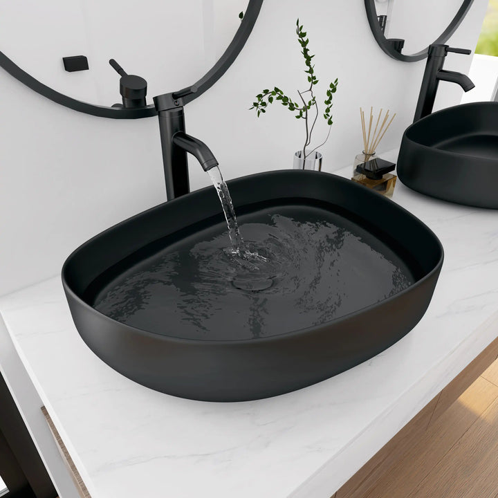 Matte black oval solid surface vessel sink with running water