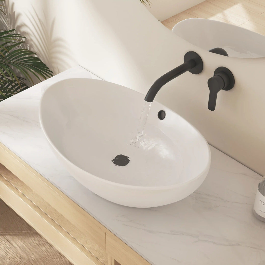 Matte white oval ceramic vessel sink with black wall-mounted faucet