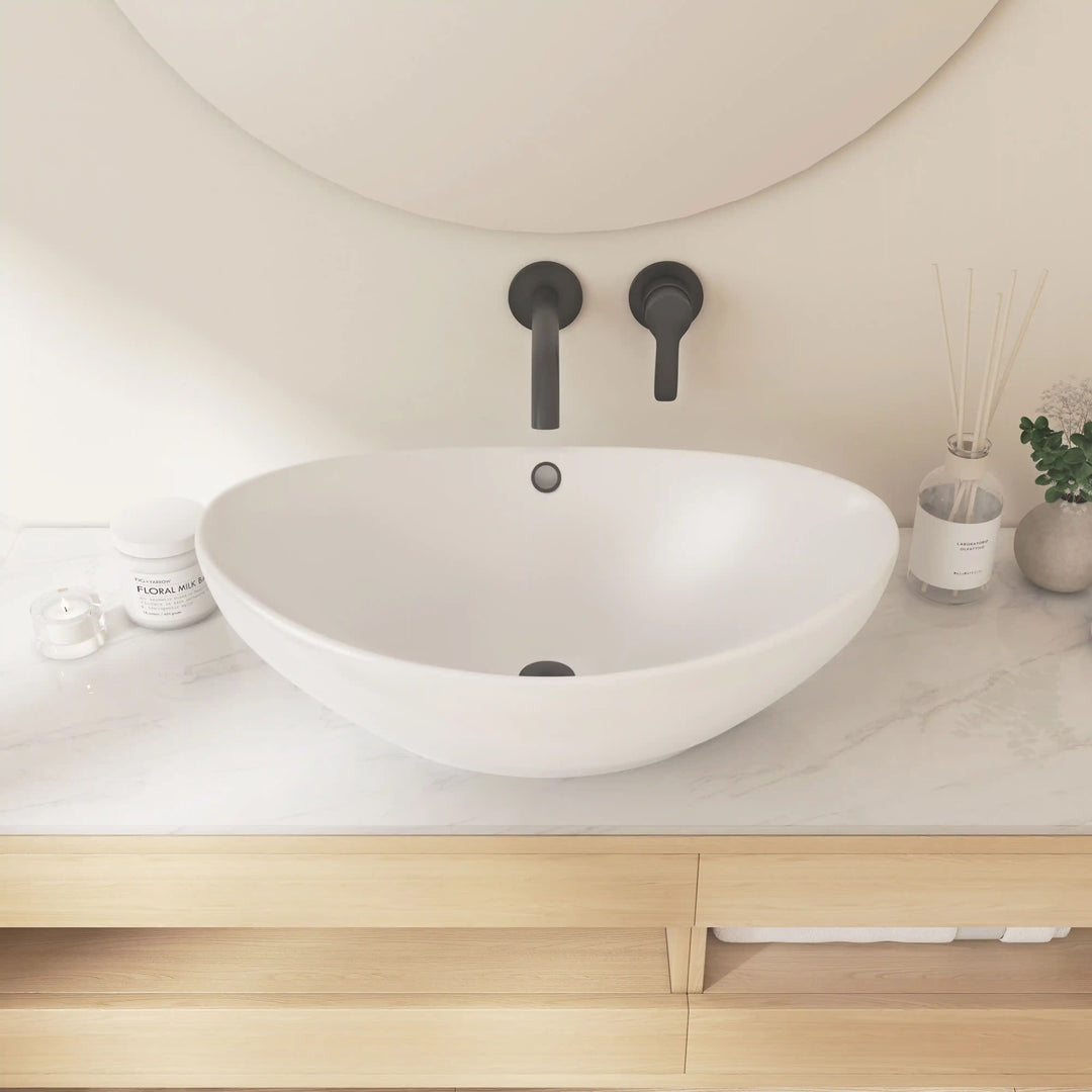 White oval ceramic vessel sink with overflow hole and wall-mounted matte black faucet