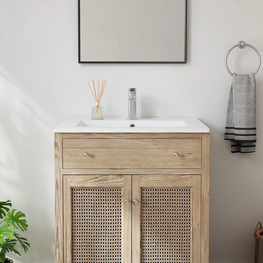 White bathroom vanity sink atop a light wood cabinet with rattan doors.